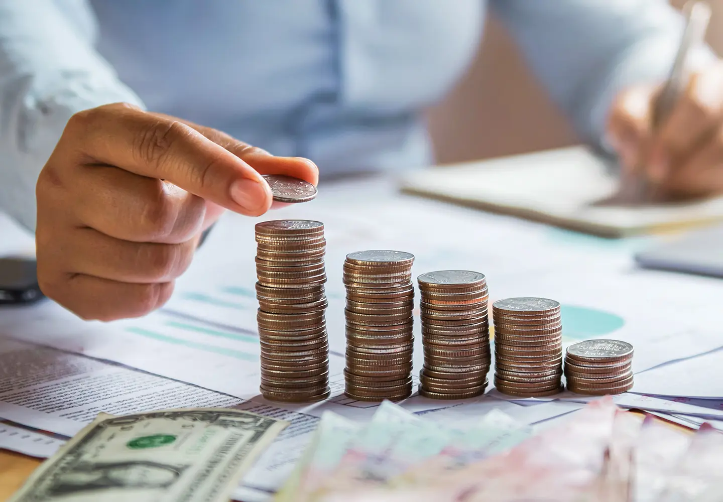 A business woman hand holding coins to stack on a desk.